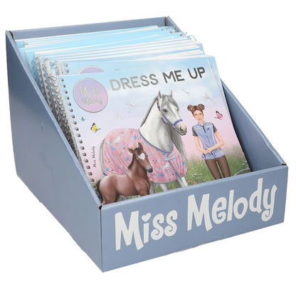 A light blue display box filled with children's books, with the front book titled 'Dress Me Up' and the box labeled 'Miss Melody'.