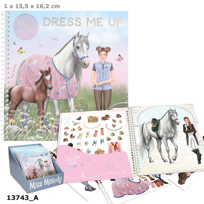Miss Melody 'Dress Me Up' sticker book set with a large illustrated cover showing a woman and horses, an open sticker sheet with various clothing and accessory stickers, a display box, and additional sticker pages on a white background.