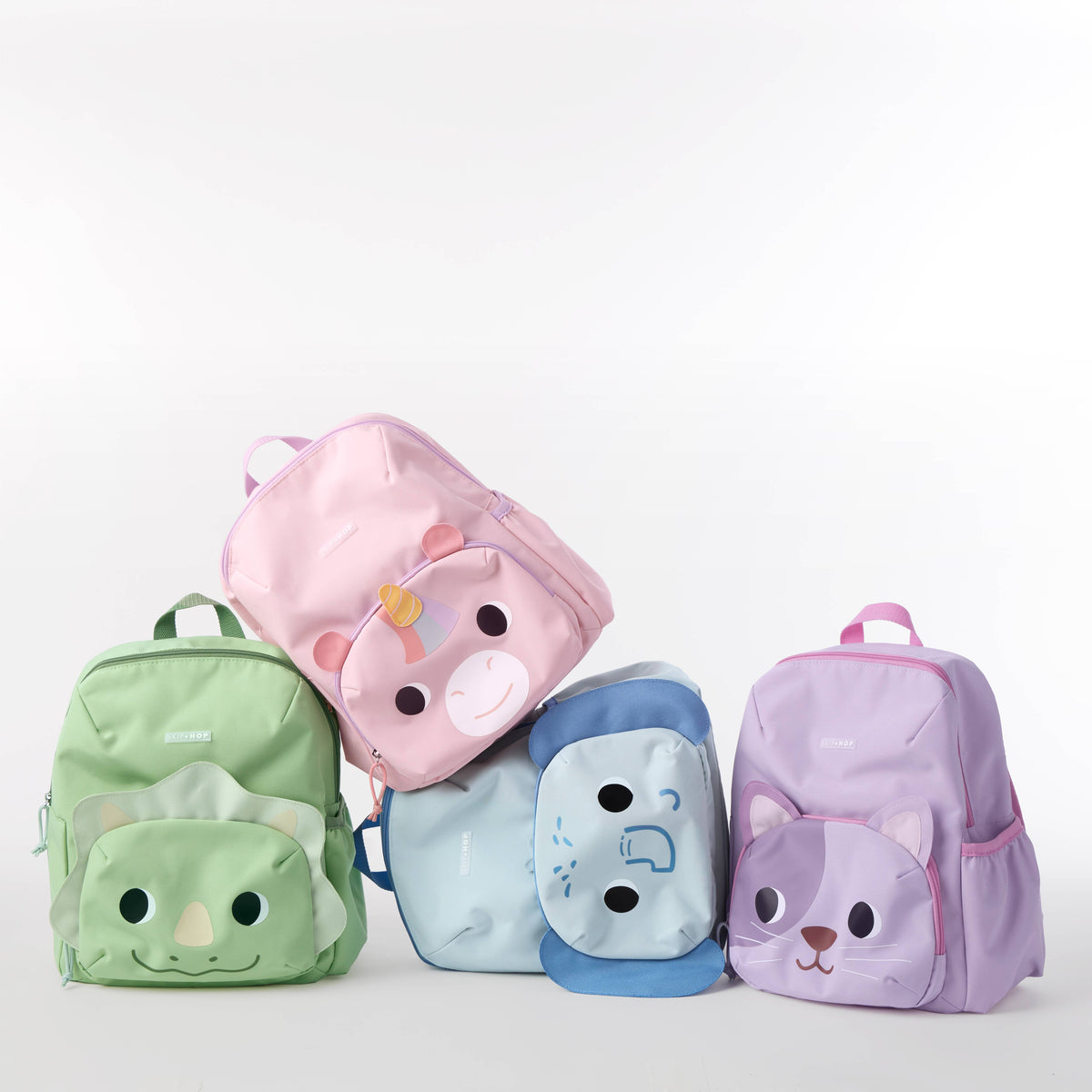 Four small children's backpacks with animal face designs, including a green dinosaur, a pink bear, a blue elephant, and a purple cat, arranged together on a white background.