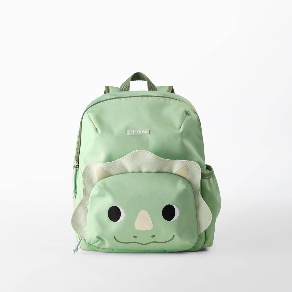 A light green backpack with a cute dinosaur face design on the front pocket, featuring black eyes, a beige nose, and a smiling mouth.