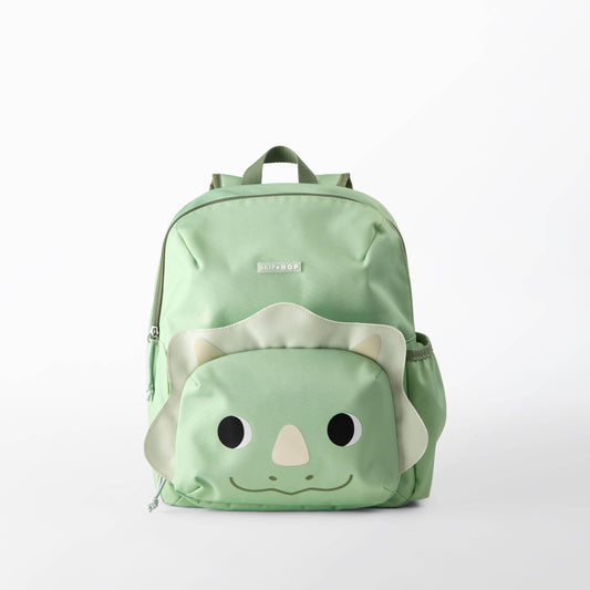 A light green backpack with a cute dinosaur face design on the front pocket, featuring black eyes, a beige nose, and a smiling mouth.